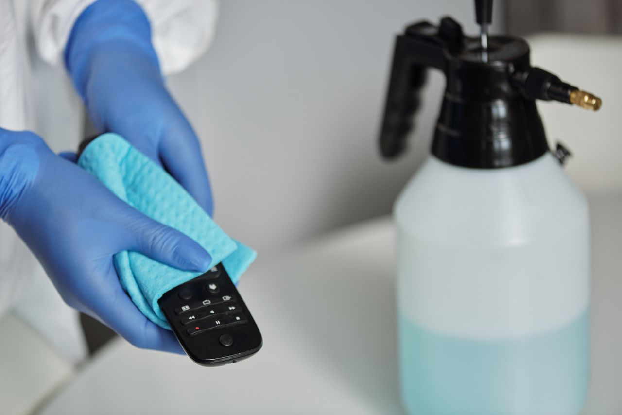 team-03 Close-up of gloved hands disinfecting a remote control with a cloth and spray bottle.